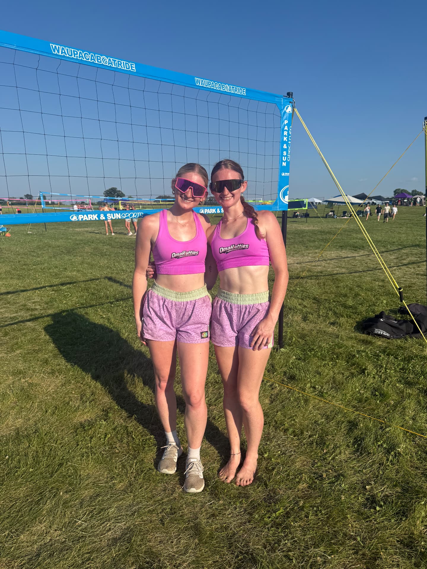 MacKenzie and Maggie, twin founders of Omahotties, in matching pink gear at a grass tournament